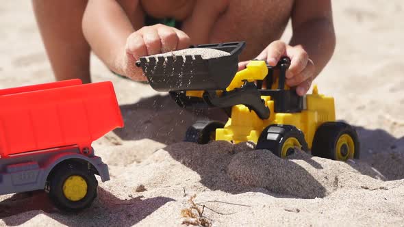 Closeup of a Child's Hands Playing in the Sand with Plastic Cars on a Sandy Beach alt