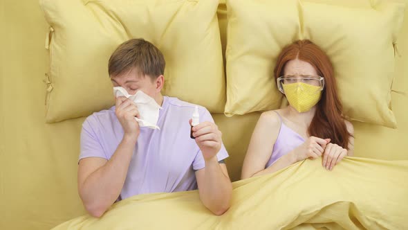 Caucasian Woman is Afraid of Catching Coronavirus or Flu Infection Lying on Bed with Sick Husband