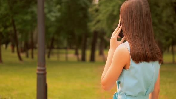 Unrecognizable Businesswoman Talking By Phone Walks Along Alley with Trees alt