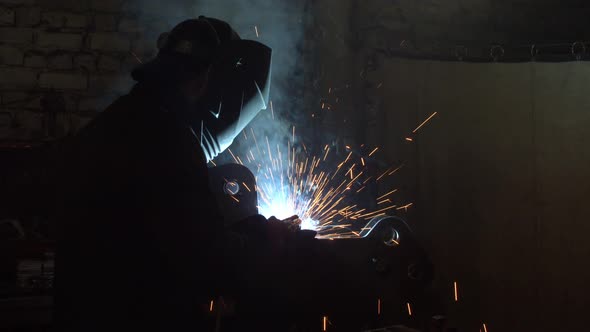 Unrecognizable Employee Welding Metal in Dark Workshop