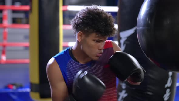 Young African Sporty Man is Practicing Box Punches Striking Punching Bag in Training Hall alt