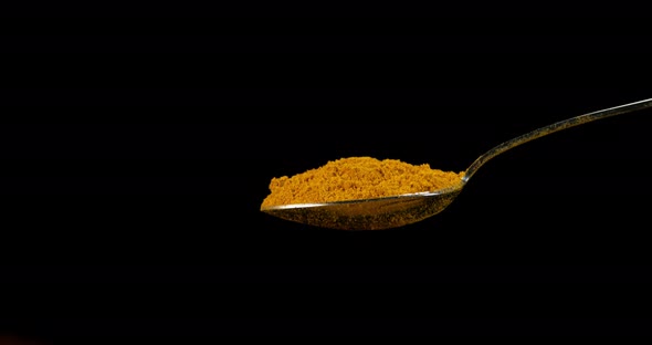 Spoon and Curry Powder falling against Black Background, Slow motion 4K alt
