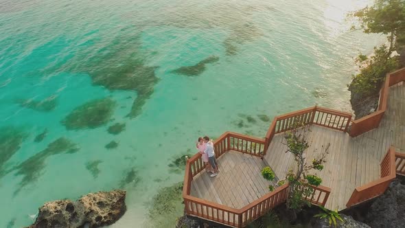 A Beautiful Light Green Coast with Reefs and a Loving Couple on the Balcony Above the Beach alt