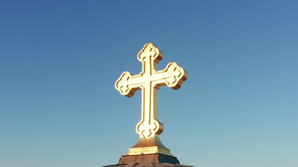 Shiny golden cross against clear blue sky. Orthodox Christian crucifix illuminated by sunlight alt