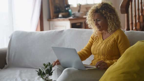 Blond woman working on laptop sitting on couch alt