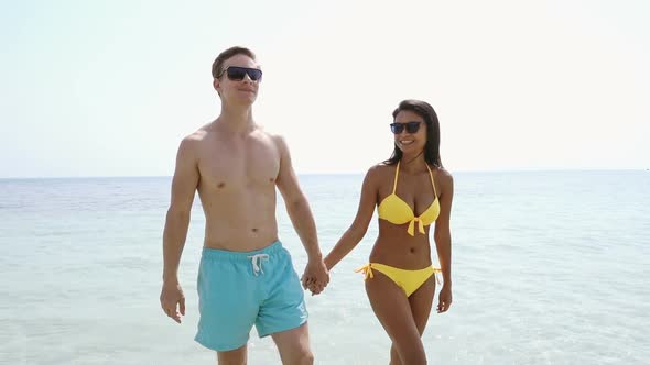 Interracial couple holding hands, walking at the beach on summer vacation