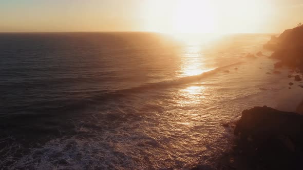 Aerial shot of rippling waves and bright setting sun near El Matador Beach, Malibu, Califronia, USA alt