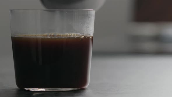 Slow Motion Pour Water Into Coffee in Tumbler Glass on Concrete Countertop with Copy Space alt