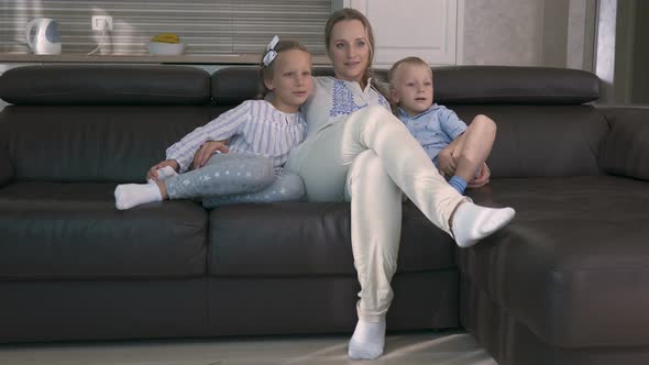 Mom and Two Children Watch TV While Sitting on the Couch