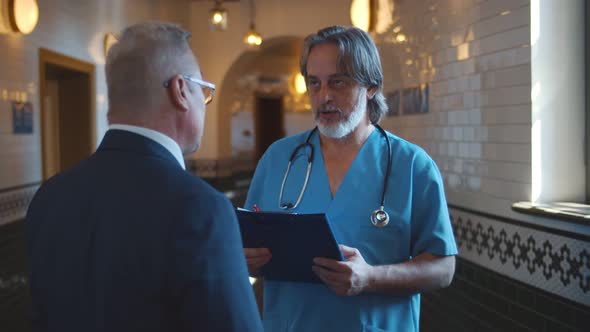 Back View of Mature Businessman Talking To Doctor in Hospital Corridor alt