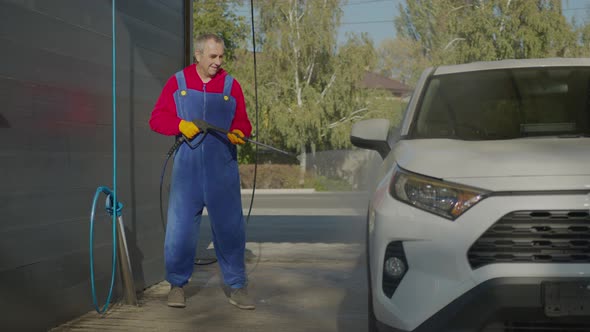 Elderly Man Washes His Car with Foam and Water. alt