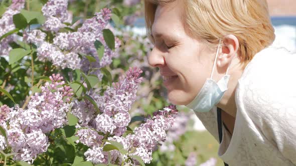 A Young Caucasian Woman Sniffs Lilac Flowers Then Sighs Sadly Puts a Protective Mask on Her Face and