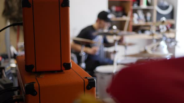 A man caucasian drummer in a garage band playing his instrument with guitar amps and music gear SLOW alt