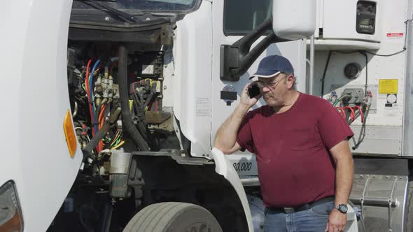 Truck driver with hood open on phone.  Fully released for commercial use.