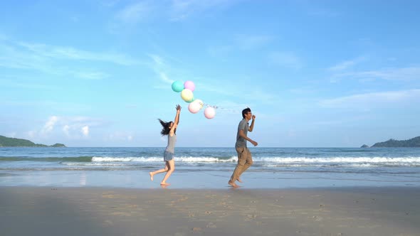 Happy Asian couple holding colorful balloons at the beach during travel trip on holidays alt