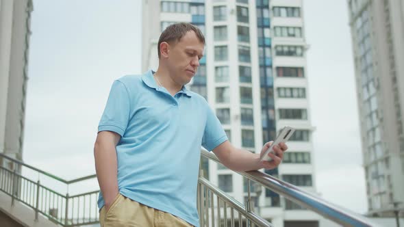 Man with a Mobile Phone in His Hands Stands on the Stairs Buildings Background alt