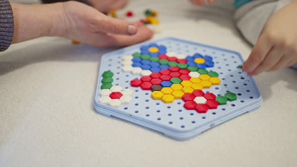Children's Hands and the Hands of an Adult Play a Colored Mosaic Laying It Out on a Substrate alt