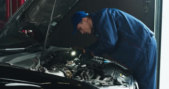 Professional Auto Mechanic Examining Car Engine, Looking Under Hood with Flashlight alt
