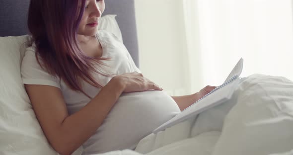 Asian pregnant wife reading a book to a child unborn baby.