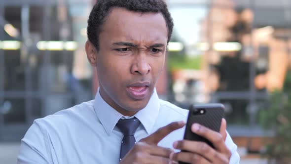Outdoor African Businessman Upset By Loss While Using Smartphone alt