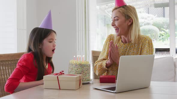 Girl blowing cake while having a video chat on laptop at home alt