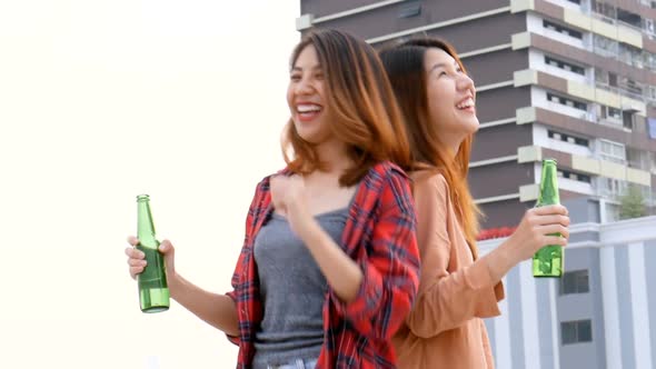 Young Asian woman lesbian couple dancing and clinking bottles of beer party on the rooftop.