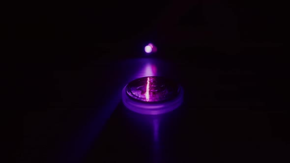 A bitcoin on a dark background is illuminated with a contrasting light and scanned by a red laser. alt