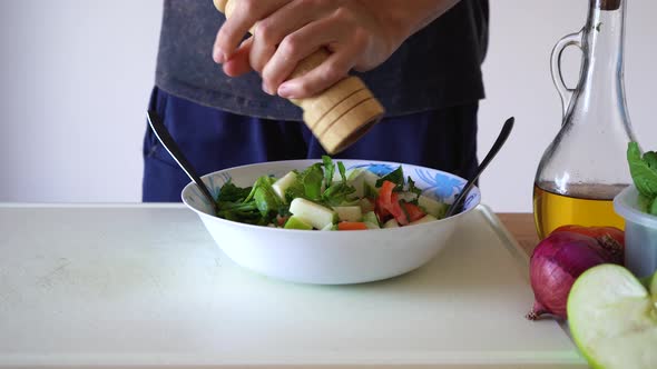Man Grinding Pepper On Healthy Salad In Kitchen. - close up alt