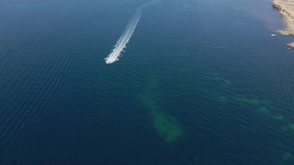 Fast Boat with People Sails Along the Rocky Coast in the Summer