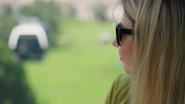 Thoughtful Woman Tourist with Sunglasses Drives Cable Way alt
