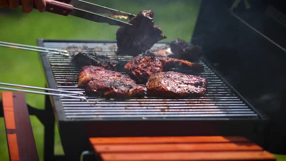 Man Flipping Barbecued Ribs on Coal Grill in His Garden