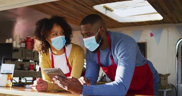African american couple wearing face masks using digital tablet in the food truck alt