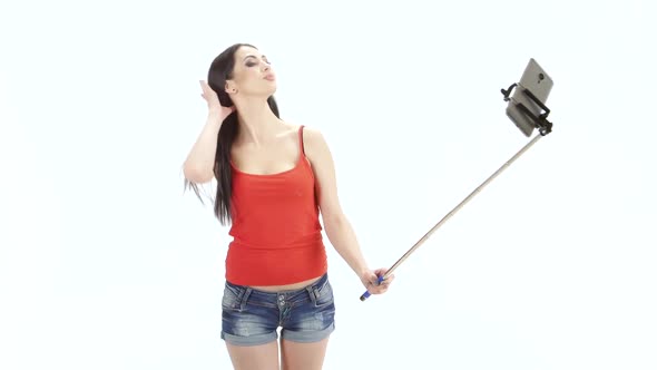 Long-haired Brunette Makes Selfie Using a Monopod. Studio. White Background alt