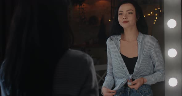 The Girl Ties Her Shirt and Begins To Straighten Her Hair Standing in Front of the Mirror.  Ultra  alt