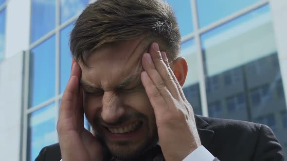 Tired Businessman Touching Head in Street, Having Bad Headache, Burnout at Work