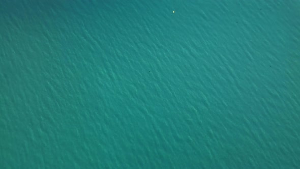 Aerial drone footage of turquoise clear water beach in early morning light, filmed with a slow tilt alt