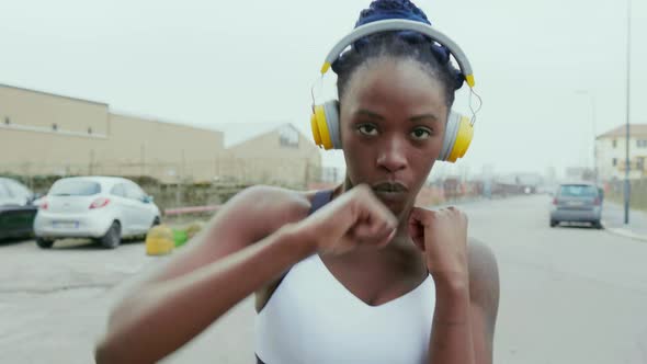 Young woman with headphones boxing in city, Milan, Italy