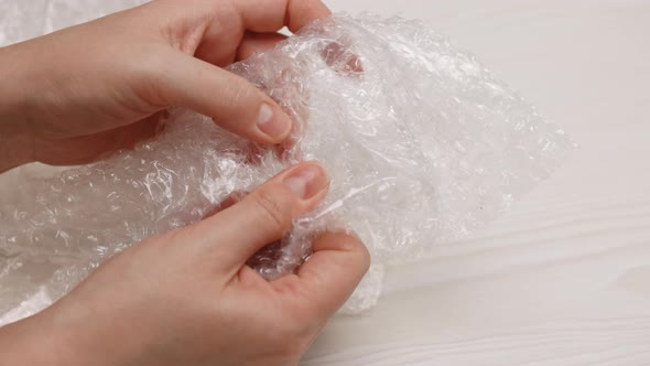 Female Hands Burst Air Bubbles on a Bubble Wrap on  White Background