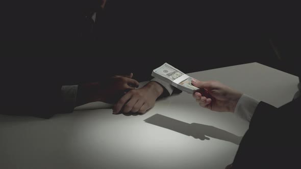 Businessman giving bribe money to his partner in dark room
