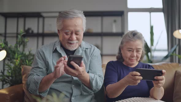 retired couple enjoy playing and competition game smartphone mobile online together on sofa
