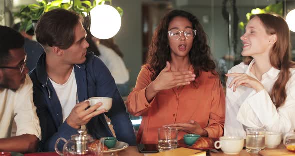 Good Looking Girl in Glasses Gesturing While Telling Funny Story Her Friends in Cosy Cafe. Cheerful