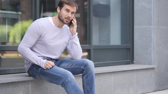 Handsome Man Talking on Phone While Sitting Outside Office Building Discussing alt