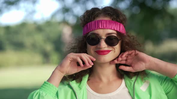 Happy Confident Woman Dancing in Summer Park Putting Down Sunglasses Winking alt