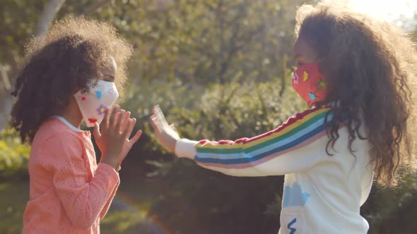 Two Afro Girls in Safety Mask Playing Hand Clapping Game Outdoors alt