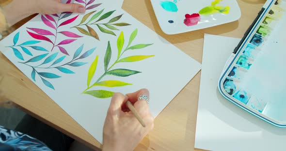 Closeup Watercolor Drawing on Paper with Brushes, Palette and Paints, Leaves on White Paper Painted. alt