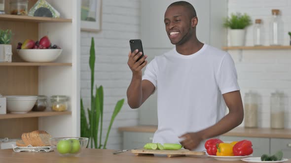 African Man Doing Video Call on Smartphone While Standing in Kitchen alt