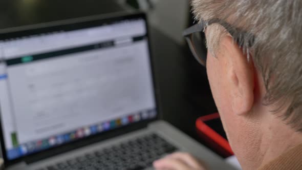 Old man in eyeglasses using laptop computer at home.