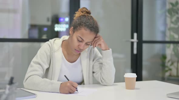 African Woman Thinking While Writing on Paper in Office alt