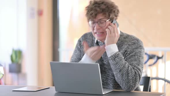 Young Man with Laptop Angry on Smartphone at Work alt