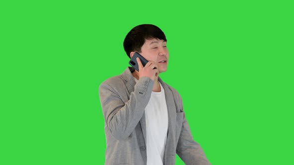 Young Asian Man Makes a Short Call with His Smartphone on a Green Screen Chroma Key alt